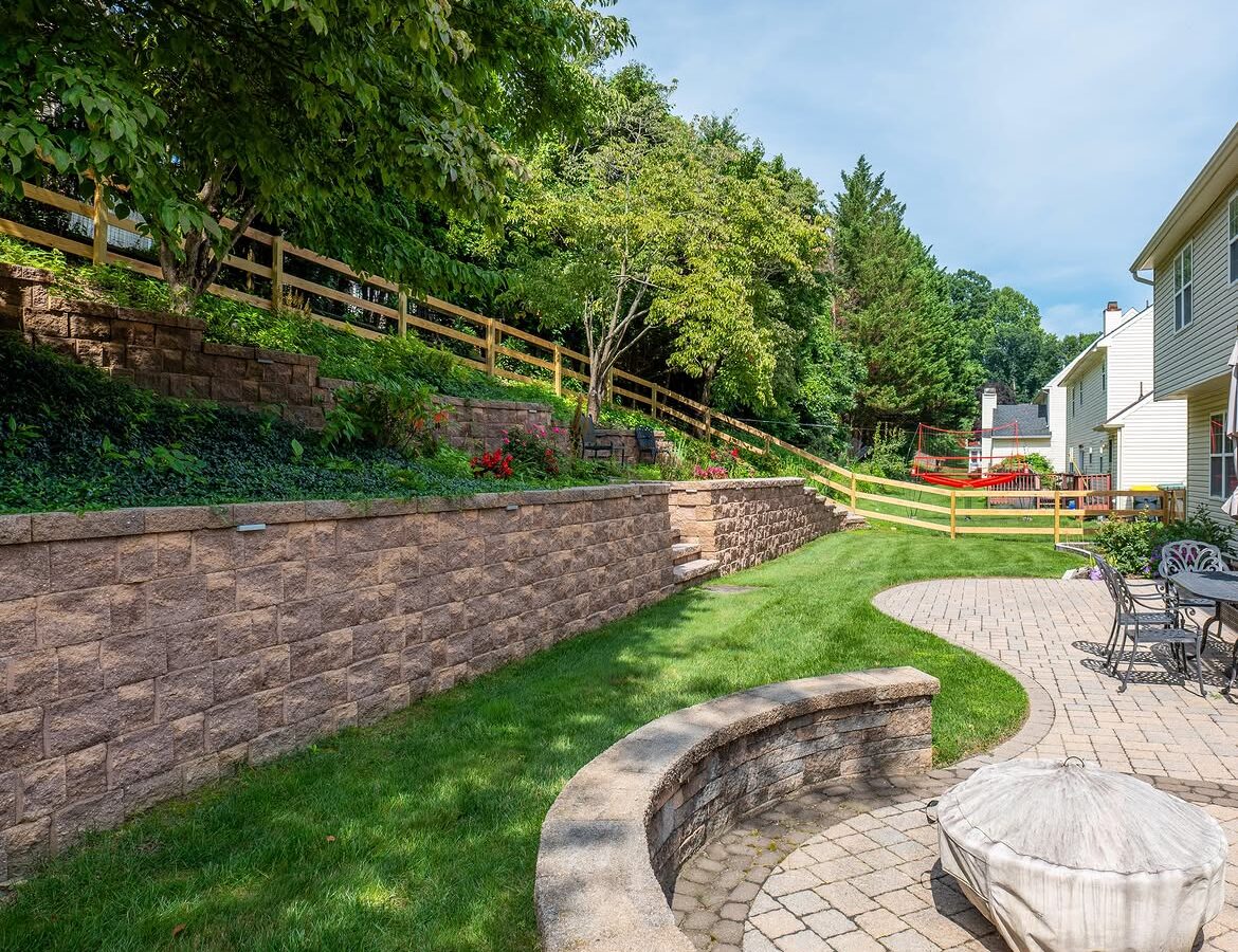 Property line view of wood post-and-rail fence, paver patio and retaining wall in Delaware